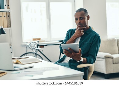 Hurrying to get things done. Thoughtful young African man in shirt working using digital tablet while sitting in the office - Shutterstock ID 1445181839