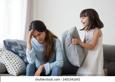 Hurt Young Mom Sit On Couch Suffer From Strong Headache Or Migraine, Little Girl Child Jump Play Near, Stressed Mother Have Problems, Have Depression Annoyed By Loud Small Daughter Ask Attention