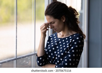 It Hurts. Exhausted Young Woman Stand Alone By Window At Home Grimace Of Sudden Pain Headache Attack Touch Forehead. Stressed Latin Female Try To Remember Recall In Memory Important Thing. Copy Space