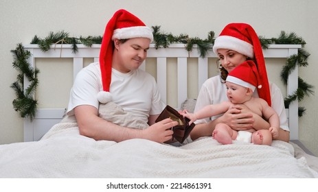 Husband With Empty Wallet Without Money And Wife With Baby On Bed Decorated For Christmas And New Year, Family Couple In Home Bedroom