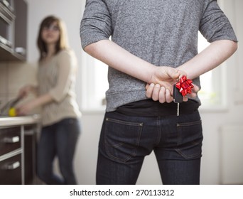 Husband Holding Gift Car Keys Behind His Back To Give His Wife