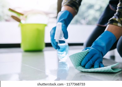 Husband housekeeping and cleaning concept, Happy young man in blue rubber gloves wiping dust using a spray and a duster while cleaning on floor at home.