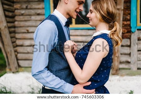 Husband hugs woman, holds in the mouth heart necklace hanging around his neck near breast against the backdrop of a wooden wall of the house. close up. love. upper half length. necklace.