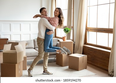 Husband Lifts Up Wife Celebrate Relocation Day To New Home. Young Married Couple Move To Bought Own Flat Feels Incredible Happy And Proud. Unpacked Carton Boxes Symbol Of Bank Loan, Mortgage Concept