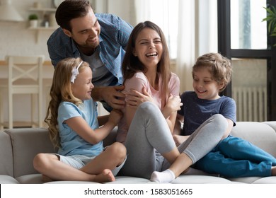 Husband with little kids tickling laughing wife people spend weekend together wearing home clothes resting living room. Concept of having fun with children active pastime at home, wealthy happy family - Shutterstock ID 1583051665