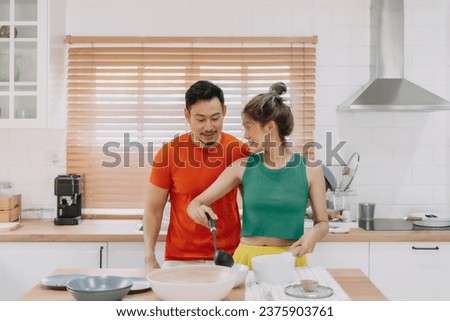 Husband looking at wife who cooking lunch for him. Happy asian couple in kitchen
