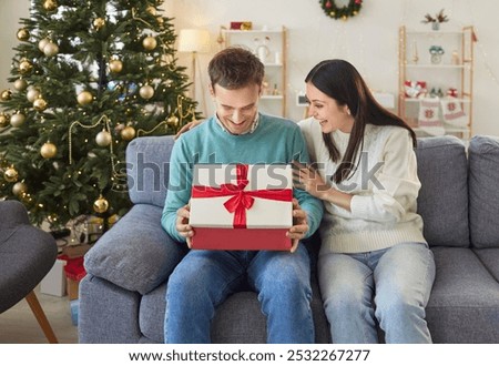 Husband opens a gift box given by wife during the Christmas or New Year celebration at home. They enjoy the holiday season, celebrating and sharing in the joy of the holiday together.
