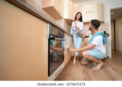 Husband Passing Detergent To Wife While Cleaning Cupboard Drawers