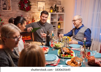 Husband Pouring Wine For His Father In Law At Christmas Celebration. Happy Family