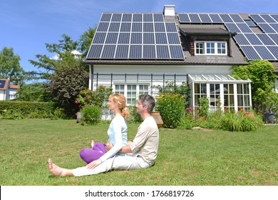 Husband And Pregnant Wife Performing Yoga In Garden Of Solar Paneled House