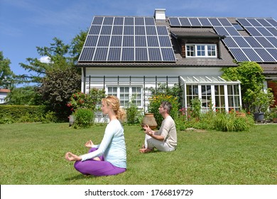 Husband And Pregnant Wife Performing Yoga In Garden Of Solar Paneled House