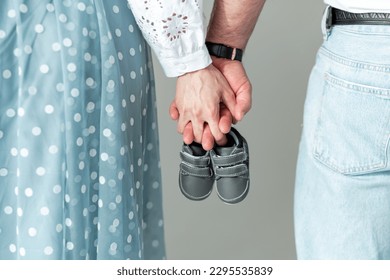 Husband and pregnant woman holding baby shoes in their hands, close-up. Motherhood, family, birth of a child - Powered by Shutterstock