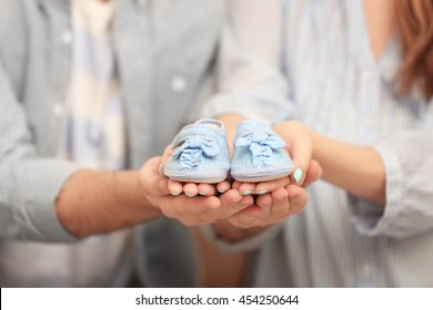 Husband and pregnant woman holding baby shoes, closeup