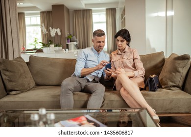 Husband Showing Photo. Handsome Husband Showing Photo On Phone To His Wife While Waiting For Plastic Surgeon