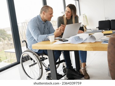 A husband, sitting in a wheelchair, works from home, supported by his wife. Together, they create an atmosphere of unity, sharing moments of joy. - Powered by Shutterstock