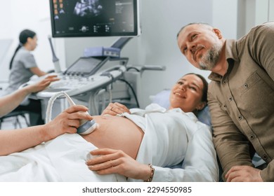 Husband is supporting his wife. Pregnant woman is lying down in the hospital, doctor does ultrasound. - Powered by Shutterstock