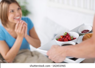 Husband Surprises Her Beautiful And Happy Wife With Breakfast In Bed Bringing Strawberries, A Croissant And Jam In A Tray