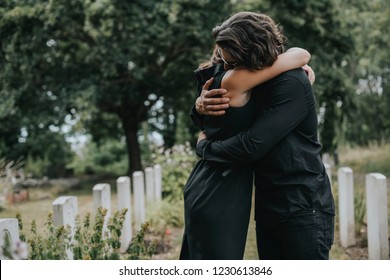 Husband trying to comfort his wife at a graveyard - Shutterstock ID 1230613846