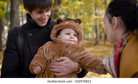 A Husband And Wife With The Baby In The Woods. The Man Took The Child In His Arms, And She Tickles The Baby's Stomach. Happy Baby Playing With Autumn Leaves