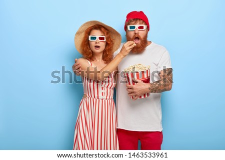 Husband and wife deeply impressed by horror film, woman feeds boyfriend with popcorn in cinema, focused at big screen enjoy loud high quality sound nice visual effects in 3d glasses. Favourite pastime
