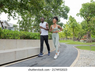 Husband and wife happy jogging run in green garden. Cheerful young couple smiling exercise in the evening summer. African American family enjoy running outdoor in the park together. Healthy lifestyle.