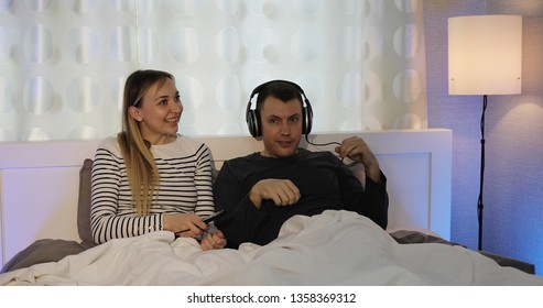 Husband And Wife In Headphones Watching TV In The Bedroom. The Family Is Having Fun And Dancing.