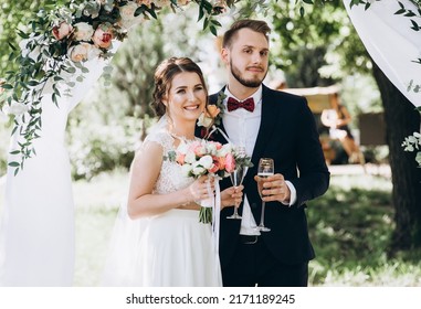 Husband and wife are holding glasses of champagne. Happy wedding photo of the bride and groom at the wedding ceremony. Wedding traditions. Newlywed. Happy together, marriage, newlyweds, wedding rings