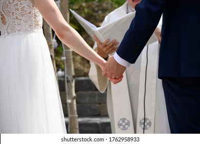 Husband And Wife Holding Hand At Their Wedding Ceremony In Front Of A Minister