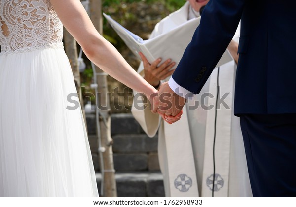 husband and wife holding hand at their wedding\
ceremony in front of a\
minister