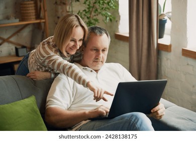 Husband and wife looking at laptop in the room. Woman pointing at screen. Middle aged couple shopping online together. Concept of fall in love, family, relationship, togetherness. - Powered by Shutterstock