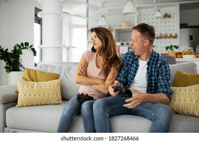 Husband and wife playing video game with joysticks in living room. Loving couple are playing video games at home - Shutterstock ID 1827268466