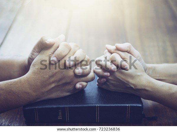 husband and wife  are praying together over holy\
bible on wooden table with the light from above with  copy space\
for your text