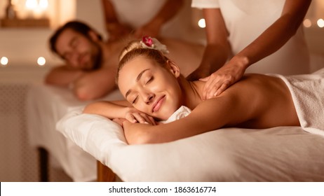 Husband And Wife Receiving Back Massage Relaxing Lying At Spa Center. Masseuses Massaging Backs During Couples Wellness Procedure. Relaxation, Beauty Treatment. Selective Focus, Low Light, Panorama