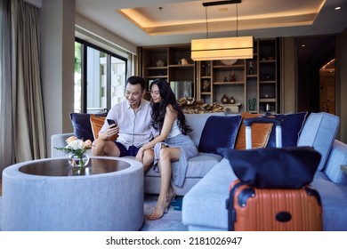 Husband And Wife Taking Selfie Photo In Hotel Room After Check-in. Happy Young Asian Couple With Suitcases Having Fun In Living Room Of Luxury Villa