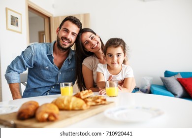 Husband And Wife With They Little Daughter Sitting At The Kitchen Table.Family Portrait.