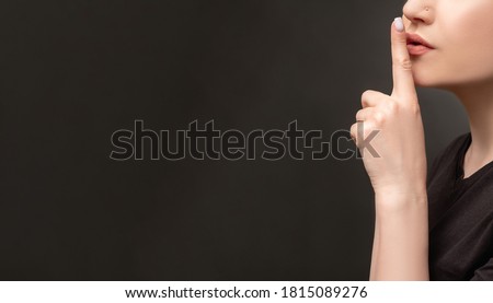 Hush gesture. Social campaign. Woman showing shhh with finger on lips isolated on black copy space ad background. Domestic violence. Family abuse. Female rights. Censorship confidential information.