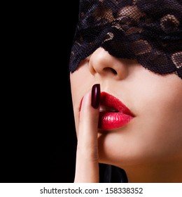 Hush. Sexy woman with finger on her red lips showing shush. Erotic girl with lace mask over black background. 