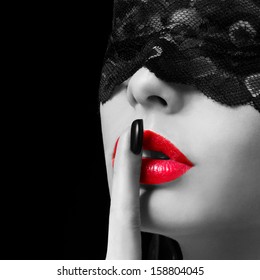 Hush. Sexy woman with finger on her red lips showing shush. Erotic girl with lace mask over black background. Black and white