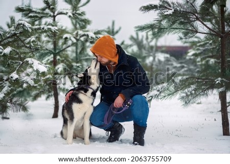 Husky dog kissing red-head bearded man in jacket in a winter forest
