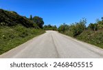 Hutch Bank Road stretches ahead, flanked by greenery under a clear blue sky, the asphalt road curves upwards and out of view in, Haslingden, Lancashire, UK