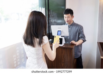 Huzhou, China 13 May 2021: cashier using digital device for payment. Man waiter calculates young woman in cafe by mobile phone via QR code of Alipay or Wechat pay (popular payment metod in China). The