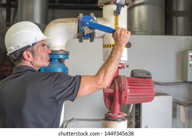 Hvac Mechanic Working On A Valve Inside Of A Boiler Room