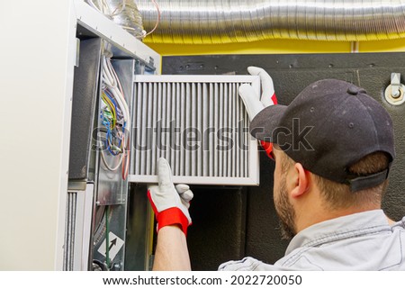 HVAC service technician changing dirty air filter in the central ventilation system. Change filter in rotary heat exchanger recuperator. Air duct ventilation system maintenance for clean air.