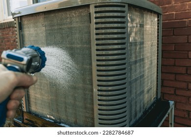 An HVAC technician cleaning an air conditioner. Rising a cooling unit with water in the spring time. An HVAC technician servicing an ac unit. A service tech cleaning a cooling system.  - Shutterstock ID 2282784687