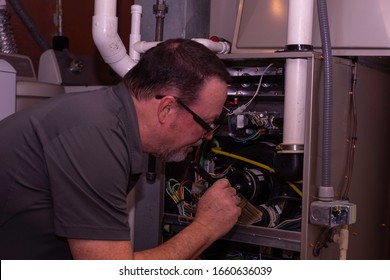 HVAC Technician Cleaning A High Efficiency Gas Furnace  Gray Shirt  