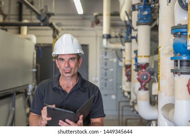 Hvac Technician Standing In A Boiler Room While Writing On A Tablet