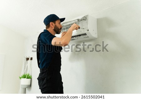 Hvac technician using a screwdriver to maintain an air conditioning unit during a service call at a residential home