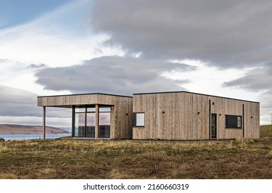 Hvammstangi, Iceland, April 30, 2022: modern house with rough wooden facade in a landscape with grassy hills and fjords under a cloudy sky
