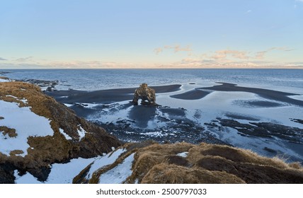 Hvitserkur rock formation standing on the icelandic coastline at sunset with a view of the snowy mountains in the distance - Powered by Shutterstock