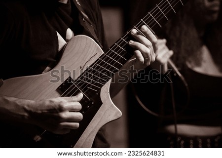 Hybrid guitar (bass and guitar), with emphasis on the guitarist's hands playing a chord. Selective focus.